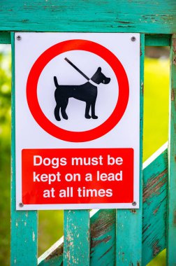 Uyarı işareti Köpekler her zaman bir ipucunun üzerinde tutulmalıdır, parkın önündeki ahşap çitlere yerleştirilmelidir.