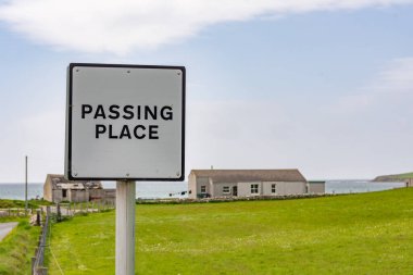 Arka planda deniz olan küçük bir köyün önünden geçerken, Shetland Adaları