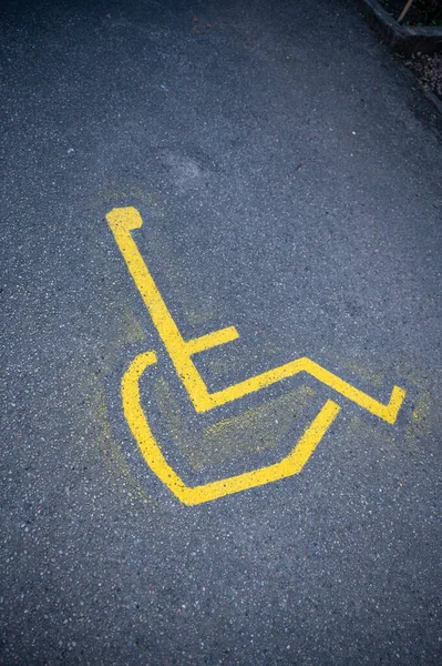 Yellow painted wheelchair sign on asphalt street, vertical shot