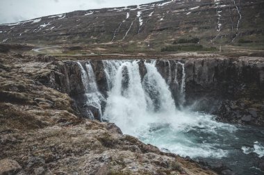 Seydisfjordur, İzlanda 'da arka planda kar dağları olan güzel bir şelale.