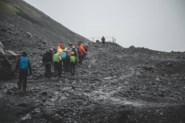 Yağmurlu havalarda, İzlanda 'da Solheimajokull Buzulu' ndan uzaklaşan bir grup insan.