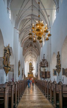 Aarhus katedralinin içinde, çatıdan sarkan avize, ahşap banklar, koridor, arka planda turist, dikey çekim, Danimarka