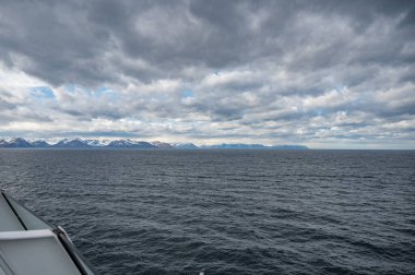 İzlanda kar dağları, deniz ve kayık güverteleriyle bulutlu hava koşullarında öndeki yolcu gemisinin tırabzanı, uzaktan görüş, geniş açılı çekim.
