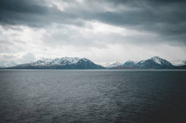 Önünde deniz olan İzlanda karlı dağları bulutlu havalarda, uzaktan görüş, geniş açı görüntüsü