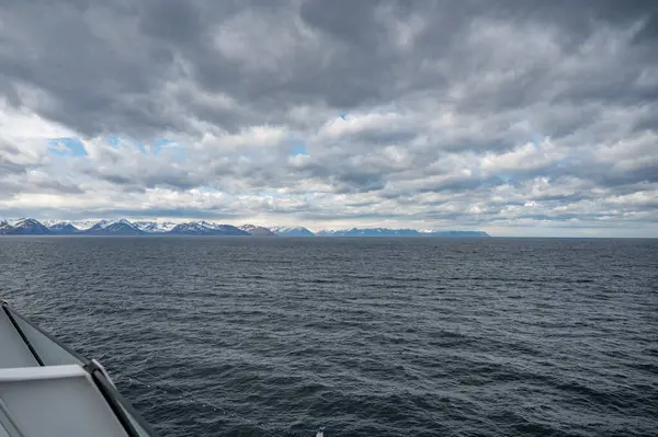 İzlanda kar dağları, deniz ve kayık güverteleriyle bulutlu hava koşullarında öndeki yolcu gemisinin tırabzanı, uzaktan görüş, geniş açılı çekim.