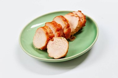 Beyaz arka planda yeşil seramik tabakta fırında tavuk göğsü..