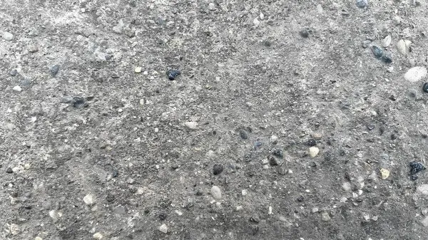 Doğal ışık altında küçük çakıl taşlarıyla dağılmış beton bir yüzeyin yakından görüntüsü..