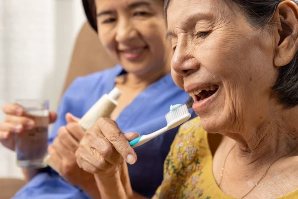 Caregiver take care asian elderly woman while brush teeth.