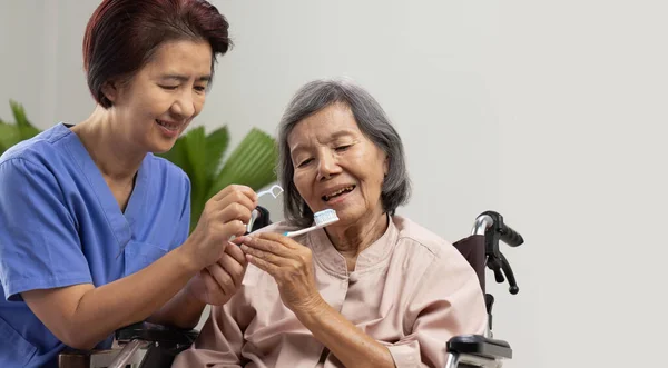 介護者はアジア系の高齢女性をケアし 歯を磨く ストックフォト