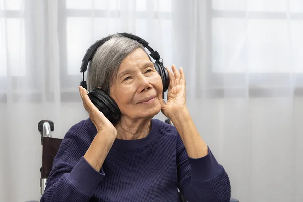 アジアのシニア女性リスニング音楽とともにヘッドフォンで自宅 ロイヤリティフリーのストック画像