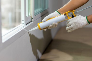 Construction worker using silicone sealant caulk the outside window frame. clipart