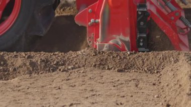 Tractor cultivating land with a rotary tiller in farm, slow motion.