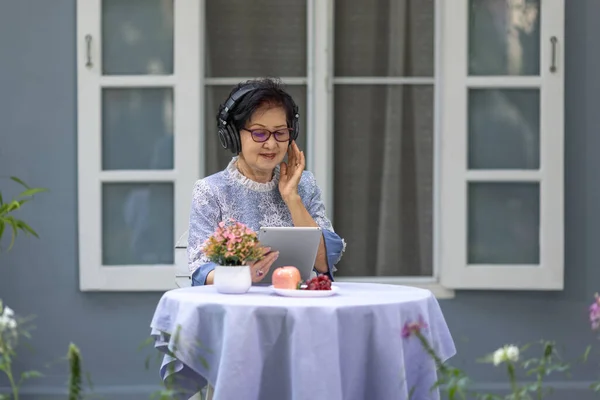 シニア女性は音楽を聞き ポーズは コンピュータタブレットを介してソーシャルメディアで良いニュースを共有しています — ストック写真