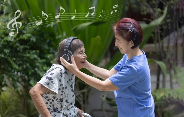 Senior woman  listening music on headphone with caregiver in backyard.
