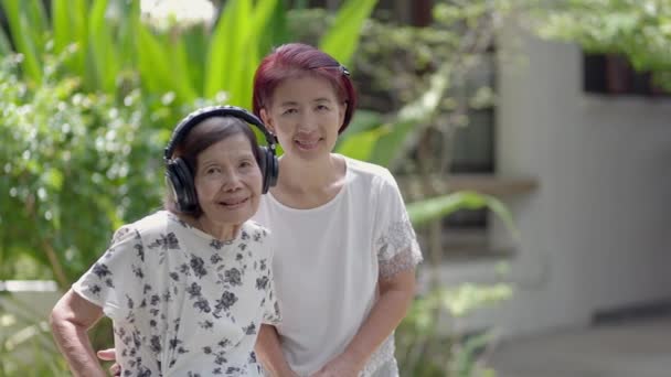裏庭で娘とヘッドフォンで音楽を聞いているアジアのシニア女性 — ストック動画