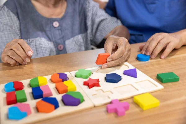 stock image Caregiver and senior woman playing wooden shape puzzles game for dementia prevention