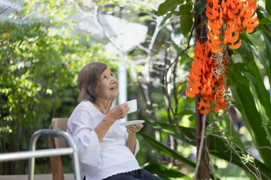 Bahçede gülümseyen yaşlı kadın. Mutlu son sınıf kadını evdeki terasta kırmızı sarmaşık çiçekleriyle rahatlıyor..