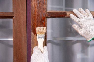 İşçi, eski tahta pencere yüzeyini zımparaladıktan sonra tahta koruyucu uygular