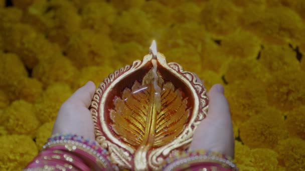 女性の手はディワリのお祝いの間にマリゴールドの上に点灯する粘土のダイヤランプを保持します — ストック動画