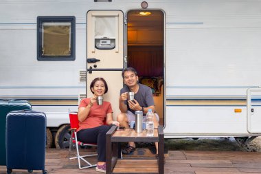 Yaşlı Asyalı çift keyifli ve rahatlar. Karavanın önünde tatilde oturuyorlar..