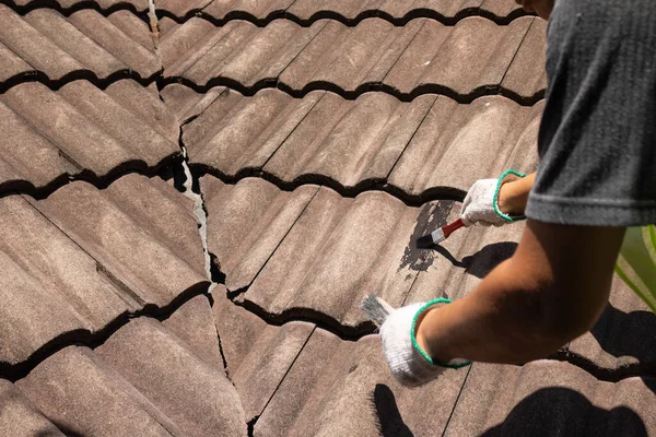 古いタイル屋根の亀裂を修正するために防水屋根コーティング修復を使用して労働者の男 ストックフォト
