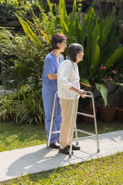 Elderly woman exercise walking in backyard with caregiver.