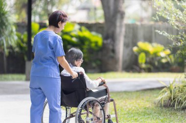 Elderly woman relaxing on wheelchair in backyard with caregiver. clipart