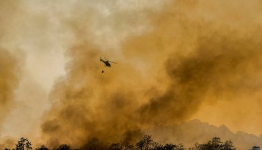 İtfaiye helikopteri orman yangınını söndürmek için su kovası taşıyor.
