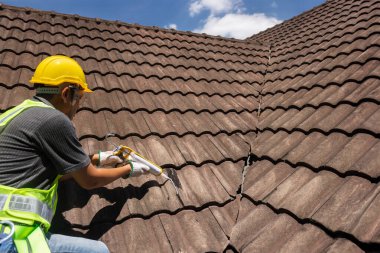 Worker man using silicone sealant adhesive  to fix crack of the old tile roof.