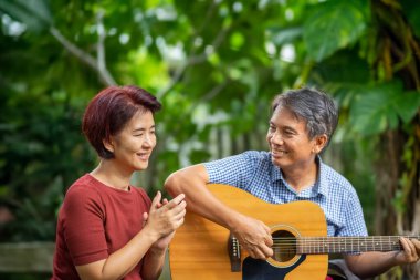 Orta yaşlı çift gitar çalarken rahatça arka bahçede bankta oturuyorlar..