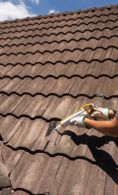 Worker man using silicone sealant adhesive  to fix crack of the old tile roof.