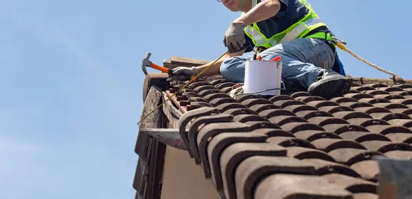 stock image Worker man repairing eaves and tile of the old roof.