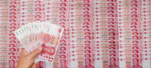 stock image Hand Holding Stack of 100 Yuan Notes Amidst Pile