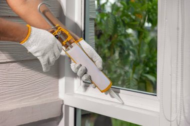 Construction worker using silicone sealant caulk for repair leaked inside window frame. clipart