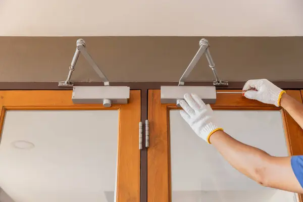 stock image Handyman fixing door closer and adjust  hydraulic arm extended.