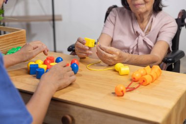 Caregiver and senior woman playing stringing beads game for dementia prevention clipart