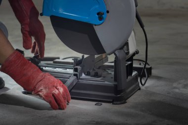 Worker cutting steel rectangular pipe in construction site.