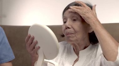 Yaşlı kadın huzurevinde yüz kırışıklıklarına ayna tutuyor..