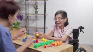 Bakıcı ve yaşlı kadın bunamayı önlemek için boncuk dizme oyunu oynuyorlar.
