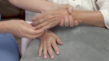 Bakıcı kadın masaj yapıyor ve kuru cilt için yaşlı eline losyon sürüyor.