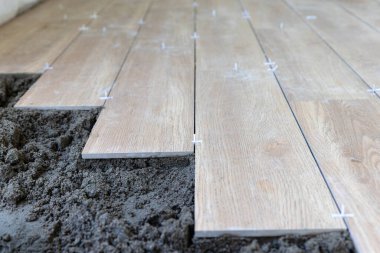 İşçi, yer kiremitlerinin doğru hizalaması için plastik fayans boşlukları kullanır, yarı kuru zemin perdeli.