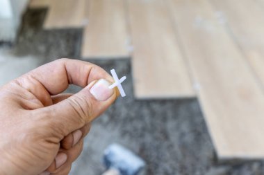 Tiler, yer kiremitlerinin doğru hizalanması için plastik fayans boşlukları kullanır, yarı kuru zemin perdelenir.