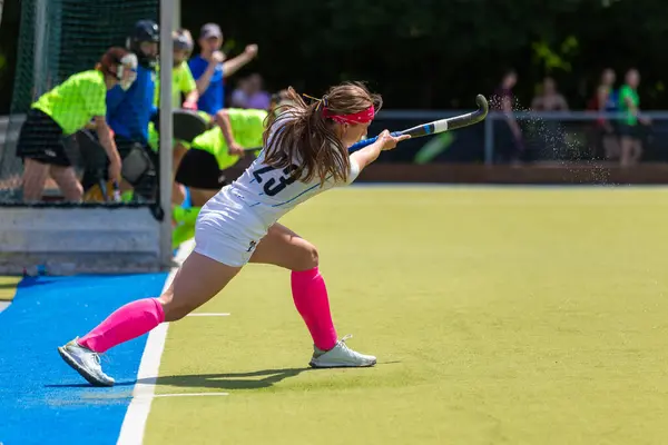 Young female field hockey player performing short corner with powerful strike