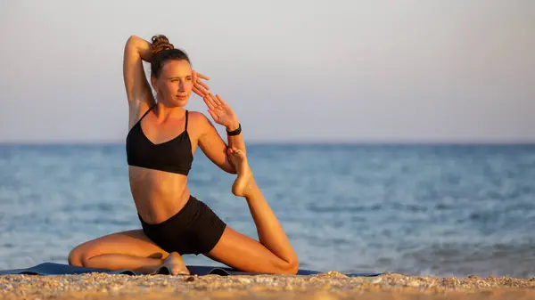 Outdoor yoga practicing at the beach. Fitness woman doing mermaid pose near the sea at sunset. Image with copy space