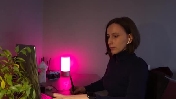 ラップトップとグラフィックのタブレットを自宅で夜に使用する若い女性 ハンドヘルドペデスタルビデオ — ストック動画