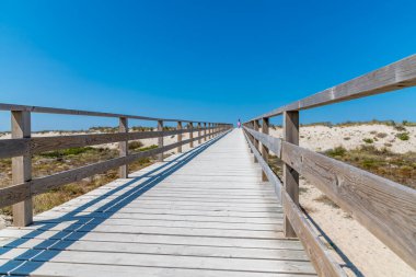 Üzerinde mavi bir gökyüzü olan uzun tahta bir sahil, Portekiz, Aveiro yakınlarındaki Costa Nova 'da yaya geçidi.