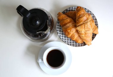 morning in a cozy apartment, on the table a kettle with fresh black coffee, a white cup and fresh croissants on a plate
