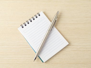 Tahta bir yüzey üzerinde boş sayfalarla sarmal kaplı bir defterin üzerine yerleştirilmiş gümüş bir kalem..