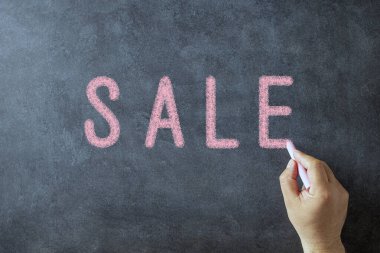 Elinde tebeşirle satışı kara tahtaya yazan bir adam. 