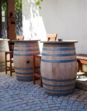 Büyük ahşap bira fıçıları sokakta masa olarak kullanılıyor ve yanlarında sandalyeler var.